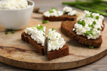 Bread with cottage cheese and green onion on wooden table, closeup