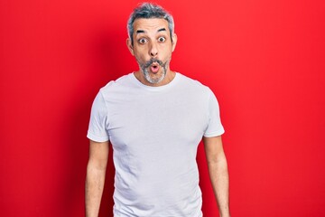Fototapeta premium Handsome middle age man with grey hair wearing casual white t shirt scared and amazed with open mouth for surprise, disbelief face