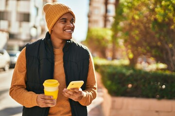 Fototapeta premium Young latin man using smartphone and drinking coffee at the city