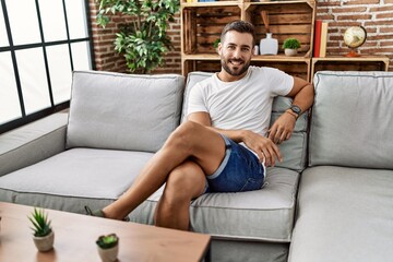 Young hispanic man smiling confident sitting on sofa at home