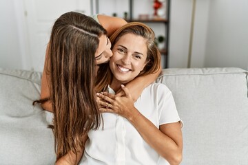 Mother and daughter kissing and hugging each other sitting on sofa at home
