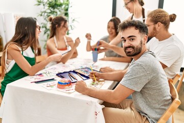 Group of young paint students smiling happy and drawing sitting on the table at art studio.