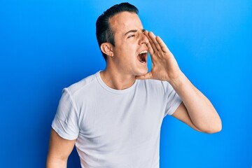 Handsome young man wearing casual white t shirt shouting and screaming loud to side with hand on mouth. communication concept.