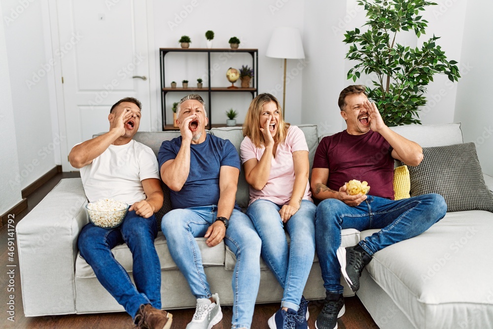 Poster group of middle age people sitting on the sofa at home shouting and screaming loud to side with hand