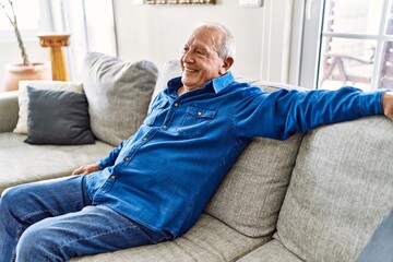 Senior man with grey hair sitting on the sofa at the living room of his house. Mature man smiling happy at home.
