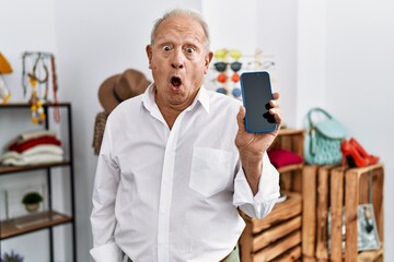 Fototapeta na wymiar Senior man holding smartphone at retail shop scared and amazed with open mouth for surprise, disbelief face