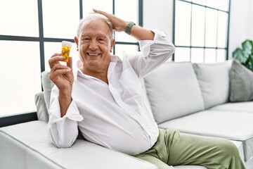 Fototapeta premium Senior man holding pills smiling confident touching hair with hand up gesture, posing attractive and fashionable