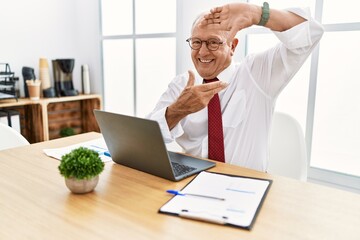 Senior man working at the office using computer laptop smiling making frame with hands and fingers with happy face. creativity and photography concept.