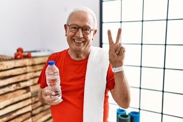 Senior man wearing sportswear and towel at the gym smiling with happy face winking at the camera...