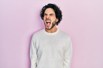 Fototapeta na wymiar Handsome hispanic man wearing casual white sweater angry and mad screaming frustrated and furious, shouting with anger. rage and aggressive concept.