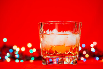 Glass of whiskey with christmas lights on red background christmas drink concept