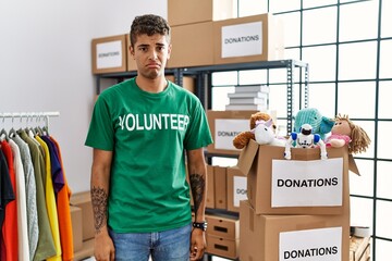 Young handsome hispanic man wearing volunteer t shirt at donations stand depressed and worry for...