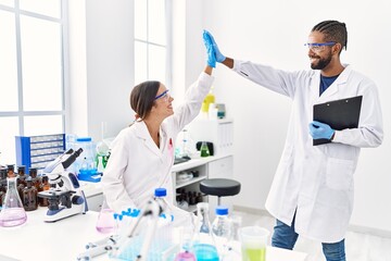 Man and woman scientist partners holding clipboard high five raised up hands at laboratory