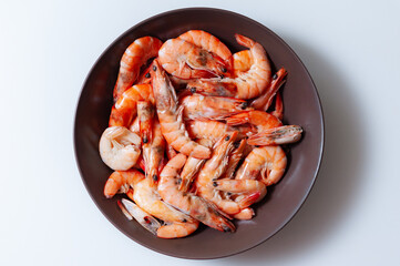 Unpeeled boiled shrimp in a dark plate on a white background