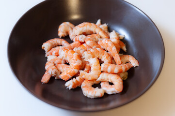 Peeled boiled shrimp on a dark plate on a white background