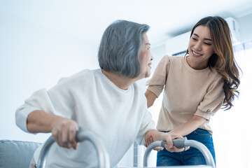 Asian young daughter support old disabled woman walk with walker at home. 