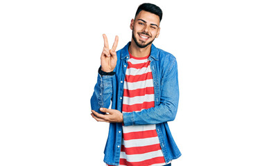 Young hispanic man with beard wearing casual denim jacket smiling with happy face winking at the...