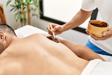 Two hispanic men physiotherapist and patient having skin back treatment using exfoliating lotion at...