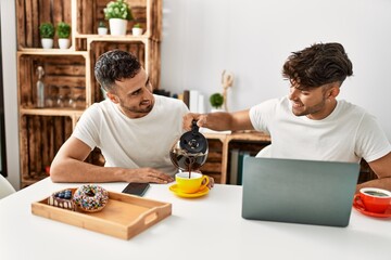 Fototapeta na wymiar Two hispanic men couple pouring coffee having breakfast at home
