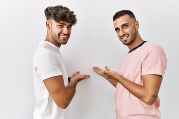 Young gay couple standing over isolated background inviting to enter smiling natural with open hand