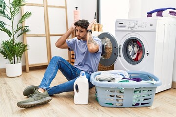 Young hispanic man putting dirty laundry into washing machine doing bunny ears gesture with hands palms looking cynical and skeptical. easter rabbit concept.
