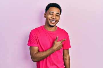 Young african american man wearing casua t shirt cheerful with a smile of face pointing with hand and finger up to the side with happy and natural expression on face
