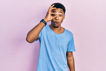 Young african american man wearing casual blue t shirt doing ok gesture shocked with surprised face, eye looking through fingers. unbelieving expression.