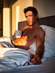 Young man shirtless on his bed with a coffee or tea cup