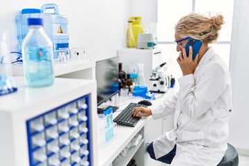 Middle age blonde woman wearing scientist uniform talking on the smartphone working at laboratory