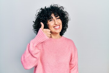 Young middle east woman wearing casual clothes doing happy thumbs up gesture with hand. approving expression looking at the camera showing success.