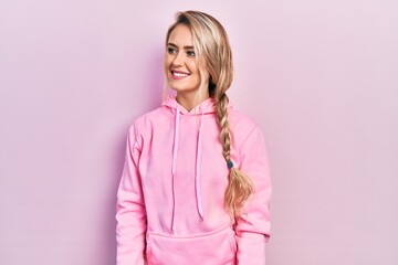 Beautiful young blonde woman wearing pink sweatshirt looking to side, relax profile pose with...