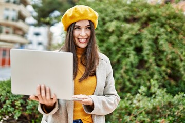 Young hispanic girl smiling happy using laptop at the city.