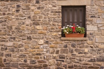 Stone facade with window detail decorated with red flowers.