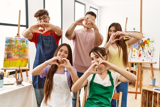 Group of five hispanic artists at art studio smiling in love doing heart symbol shape with hands. romantic concept.
