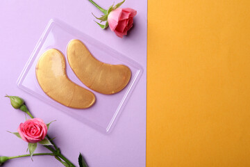 Under eye patches and rose flowers on color background, flat lay with space for text. Cosmetic product