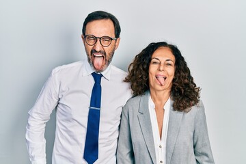 Middle age couple of hispanic woman and man wearing business office uniform sticking tongue out happy with funny expression. emotion concept.