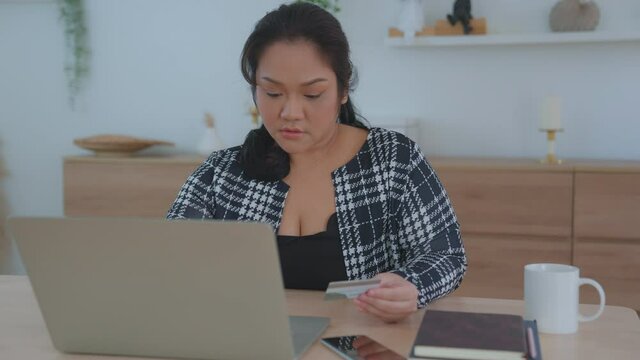 A large, plump, chubby Asian Female ordering online by paying via credit card payment system. The woman was disappointed that she was unable to reserve the items she needed. online shopping concept.