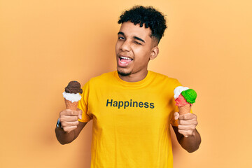Young african american man wearing t shirt with happiness word message holding ice cream winking...