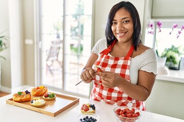 Hispanic brunette woman preparing pastries with strawberry at the kitchen