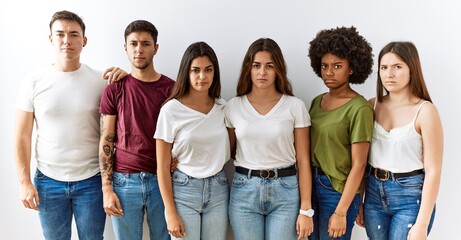Group of young friends standing together over isolated background skeptic and nervous, frowning...