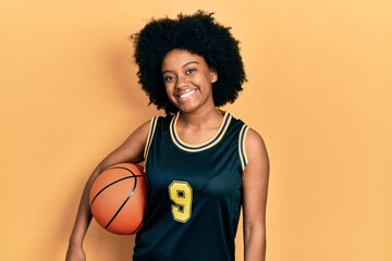 Young african american woman holding basketball ball looking positive and happy standing and smiling with a confident smile showing teeth