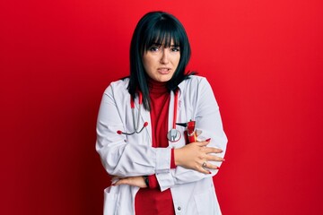 Young hispanic woman wearing doctor uniform and stethoscope shaking and freezing for winter cold...