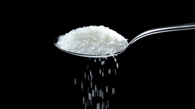 Sugar falling from spoon in slow motion on black background