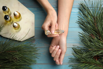 Woman applying pine essential oil on wrist at light blue wooden table, top view