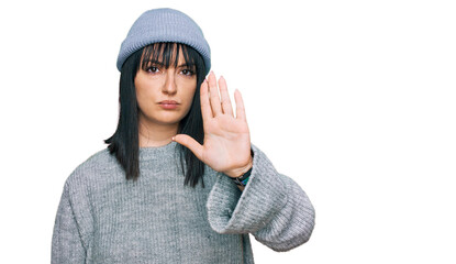 Young hispanic woman wearing cute wool cap doing stop sing with palm of the hand. warning...