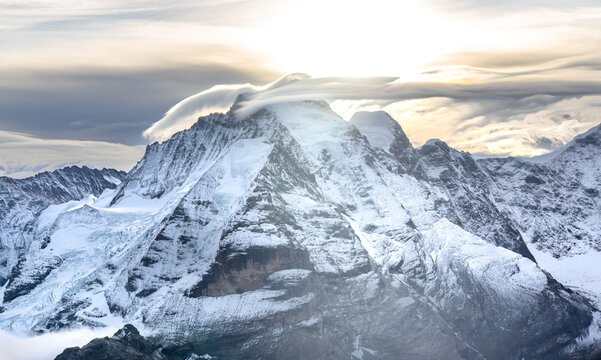 View of the famous peaks Jungfrau, M&ouml;nch and Eiger from the Schilthorn in the Swiss Alps over the Lauterbrunnen Valley at sunrise with dramatic clouds and fresh snow.  
