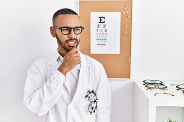 African american optician man standing by eyesight test thinking worried about a question, concerned and nervous with hand on chin