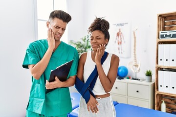 Physiotherapist working with patient wearing arm on sling at rehabilitation clinic touching mouth with hand with painful expression because of toothache or dental illness on teeth. dentist concept.