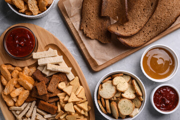 Different crispy rusks and dip sauces on light marble table, flat lay