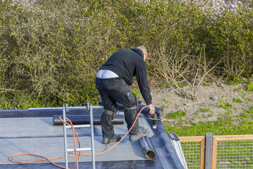 A roofer installing roofing felt with a propane blowtorch